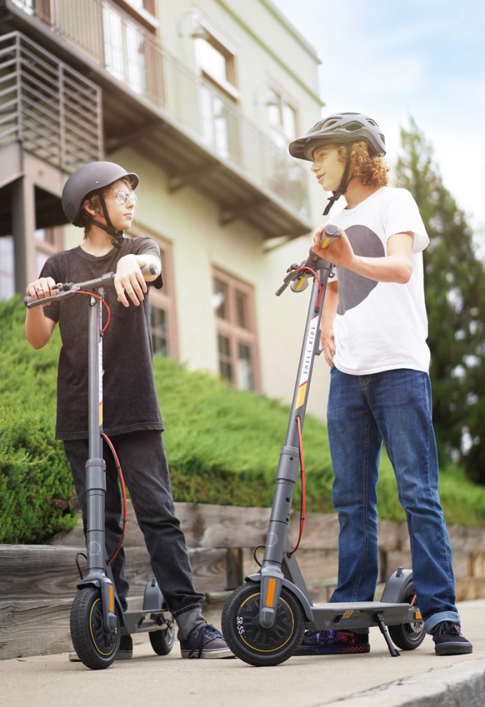 two teenage boys talking next to two electric scooters